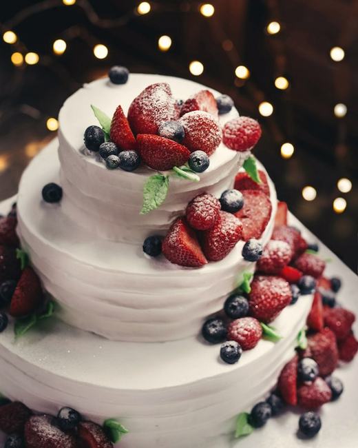 Two-tier white cake decorated with fresh strawberries and blueberries
