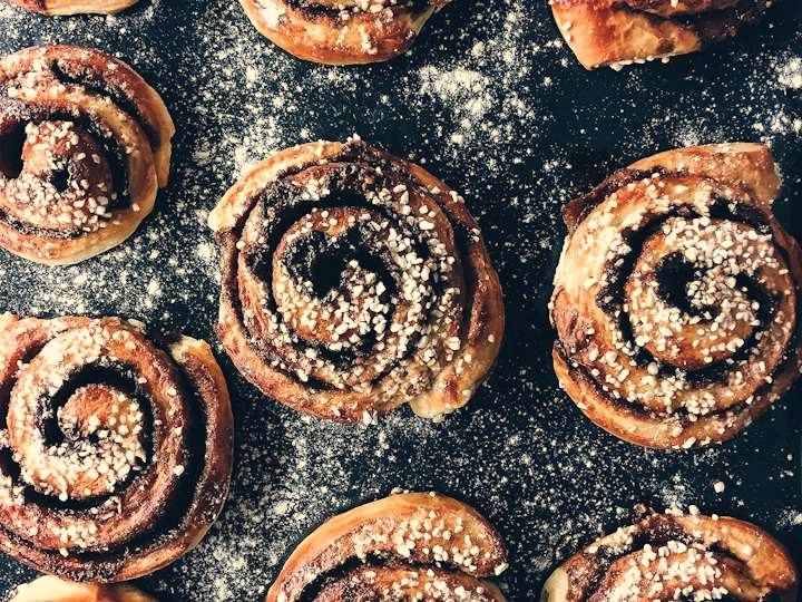 Cinnamon buns topped with pearl sugar on a dark floured surface