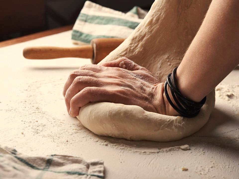 Baker's hands kneading dough on a floured wooden table