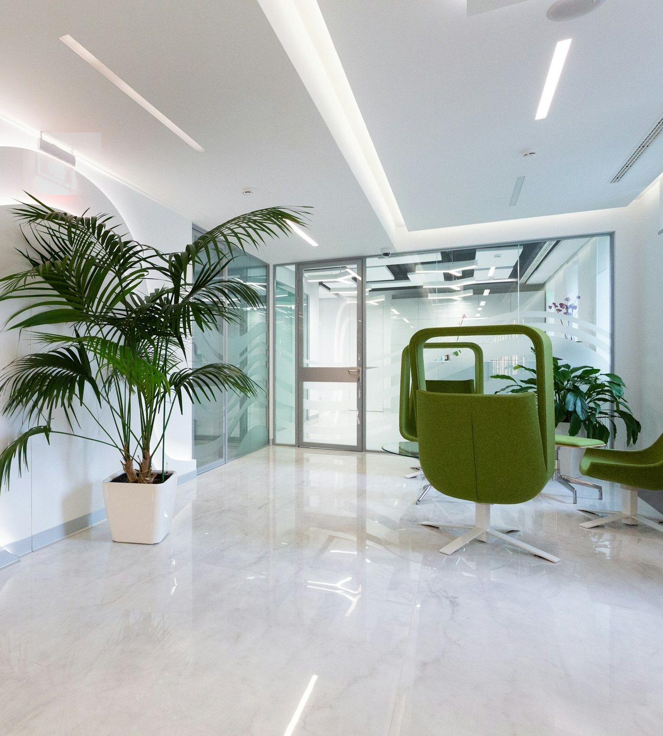 A calm, light-filled reception with marble floor, a palm and soft green armchairs