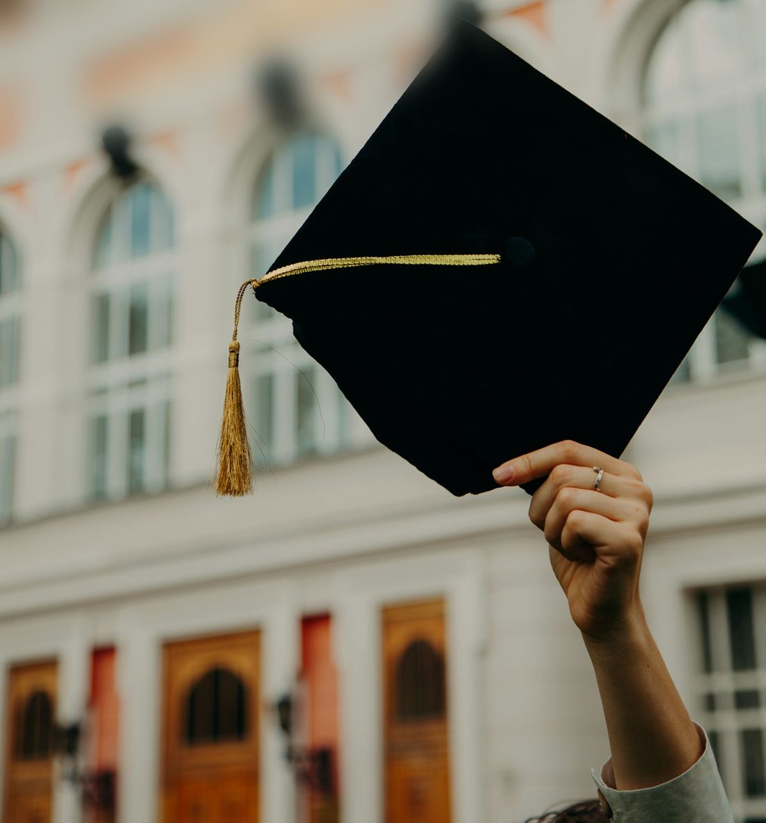 A graduate raising a mortarboard outside the main building at convocation