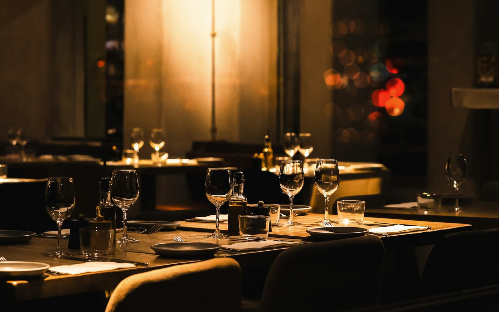 Window tables laid for dinner, glasses catching the lamplight