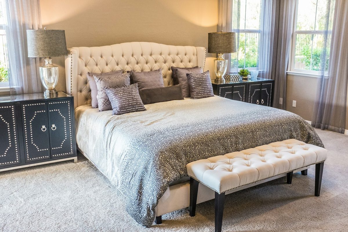 A tufted headboard bed between lamps, garden light through tall windows