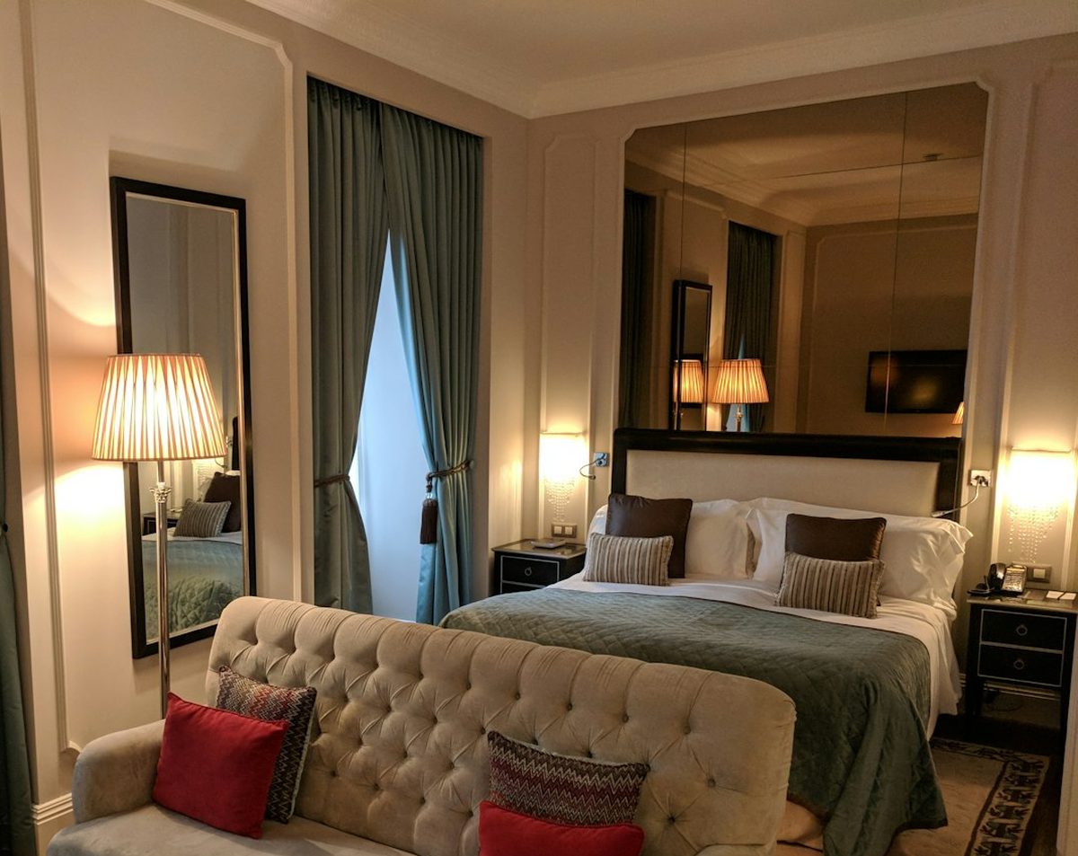A suite with a tufted sofa, a lamplit bed and tall teal curtains
