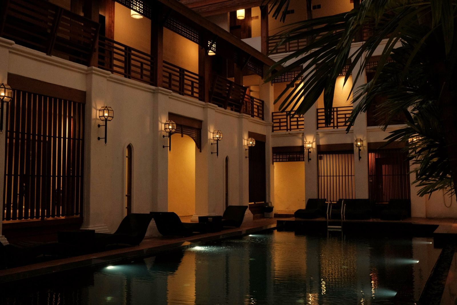 A boutique hotel courtyard at blue hour, with lanterns along the arcade and a still pool
