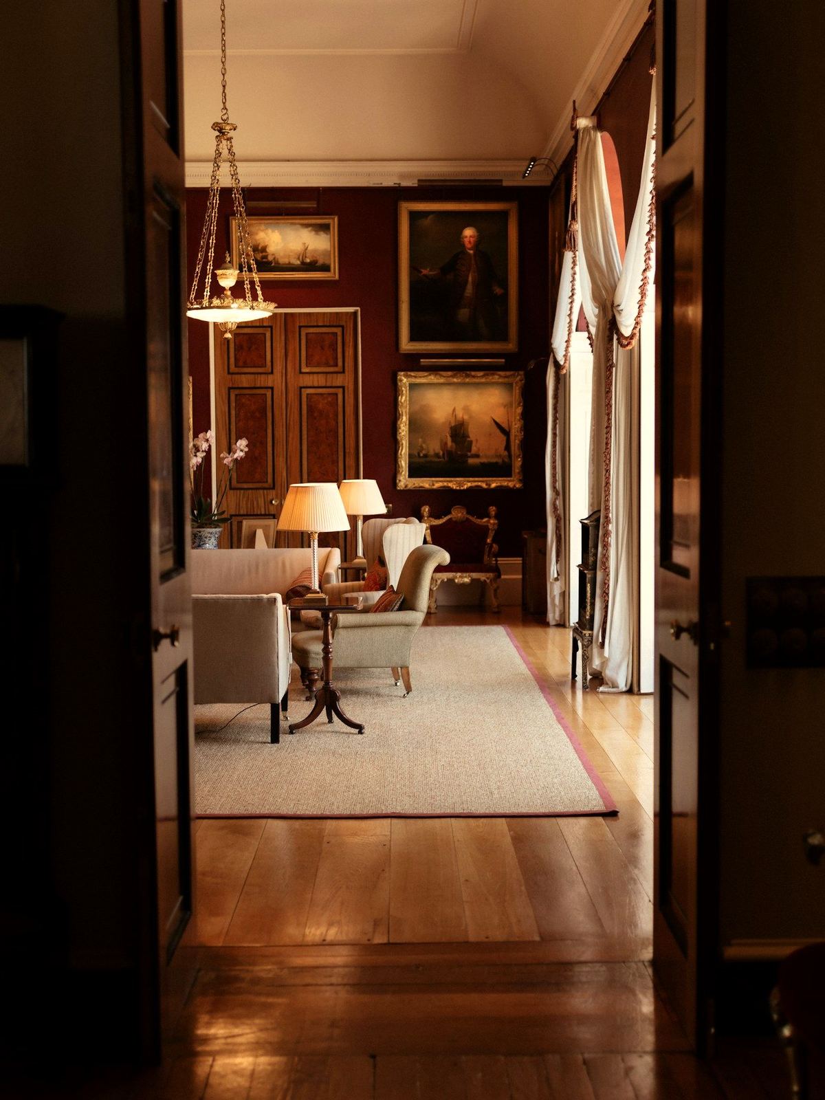 View through tall timber doors into a lamp-lit drawing room
