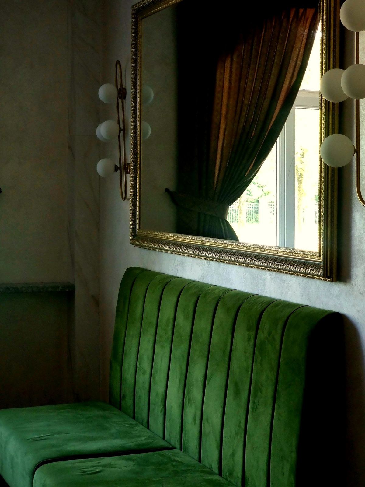 A bottle-green velvet banquette beneath a gilt-framed mirror