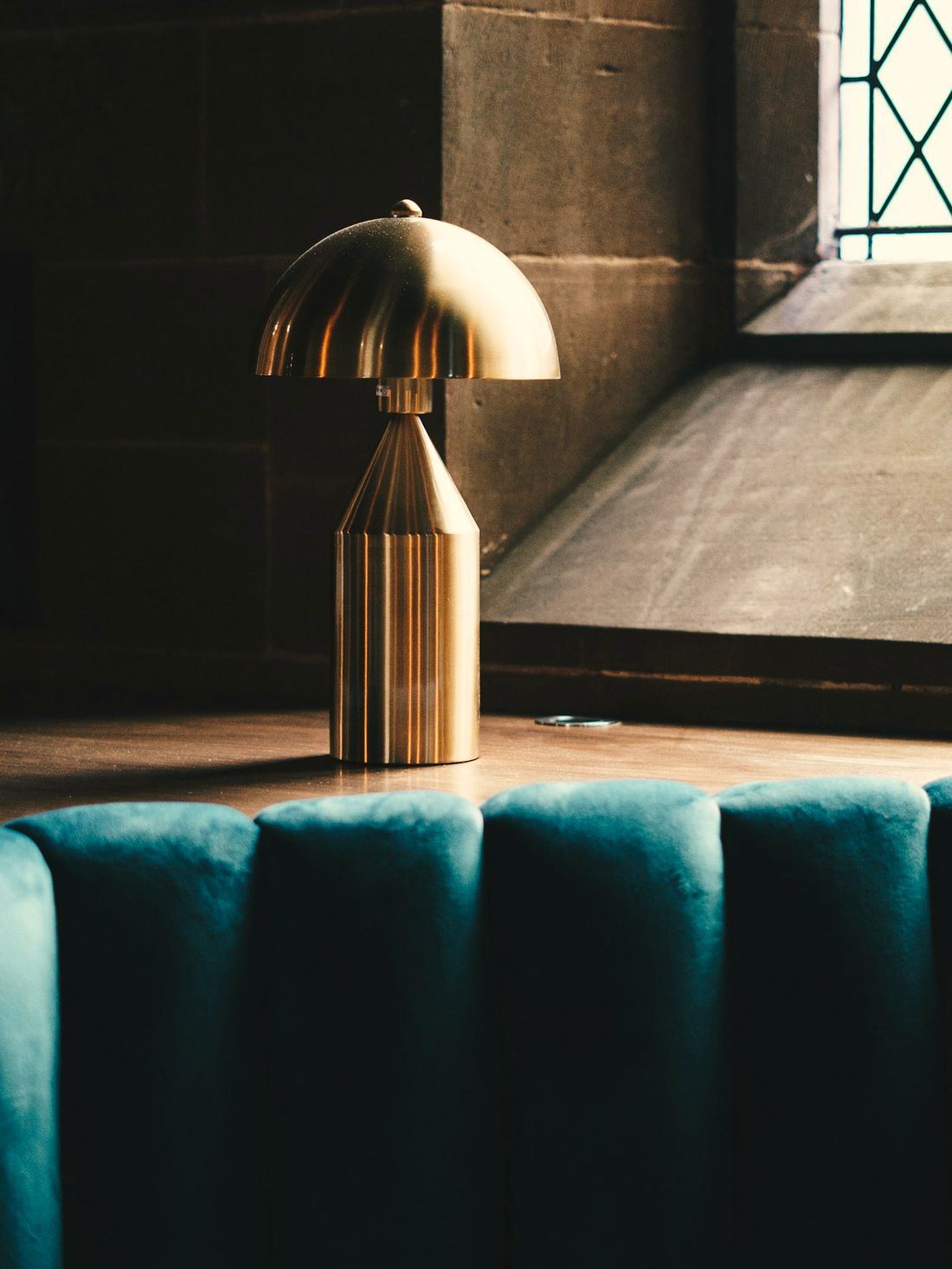 A fluted brass table lamp on a deep teal velvet banquette
