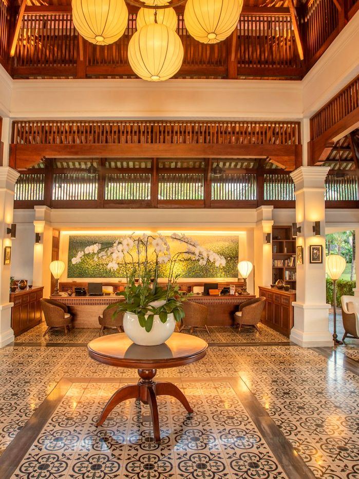 An open timber-roofed hotel lobby with lanterns, rattan chairs and patterned tiles