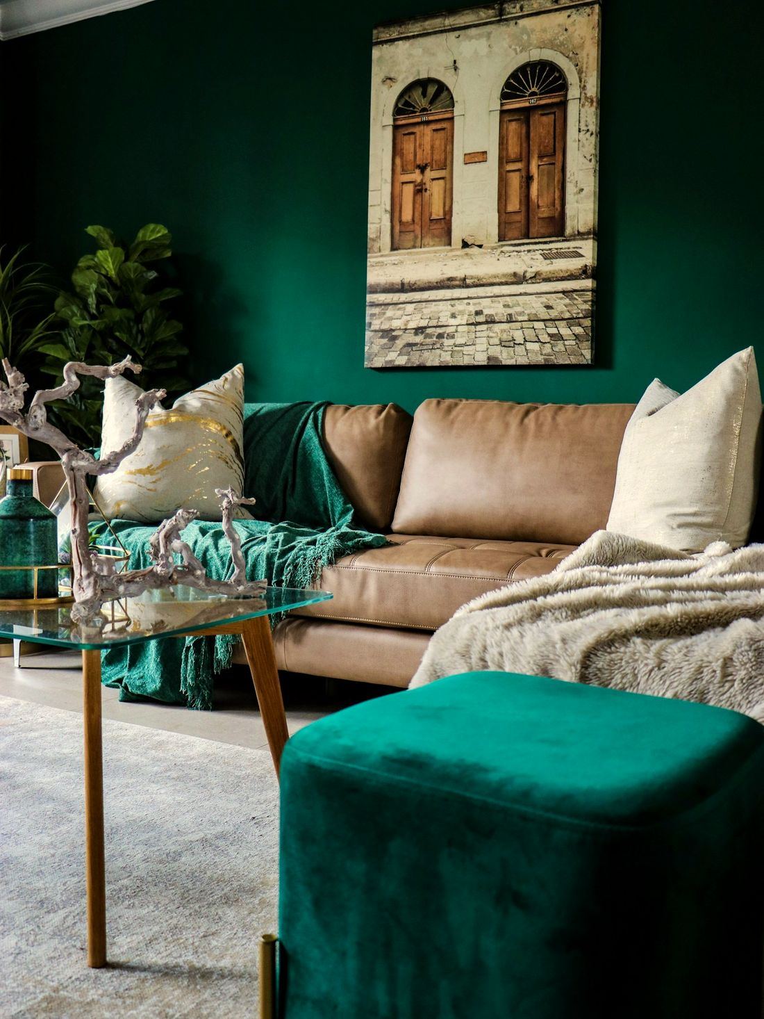 A living room with a bottle-green wall, leather sofa and green velvet ottoman