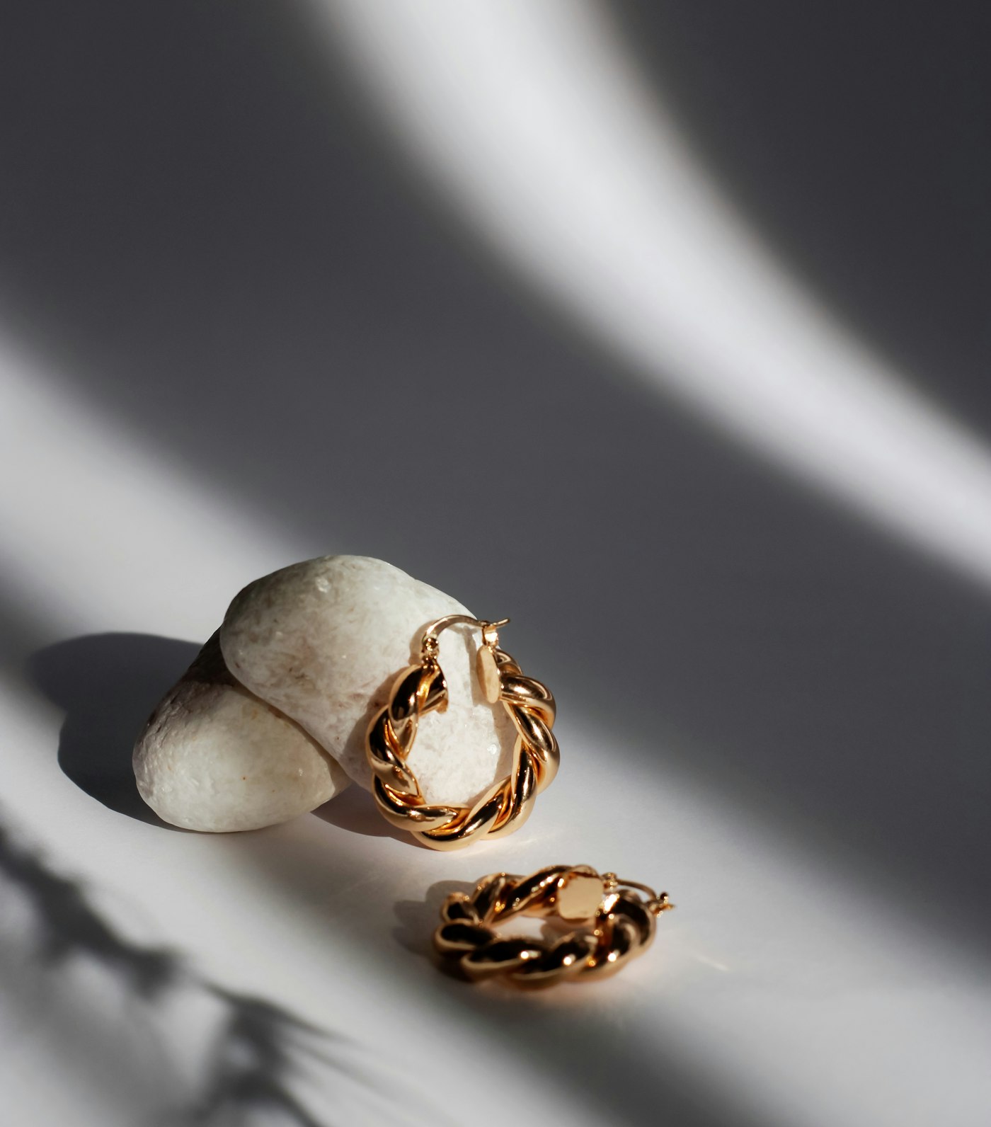 Twisted gold hoop earrings resting on a pale pebble